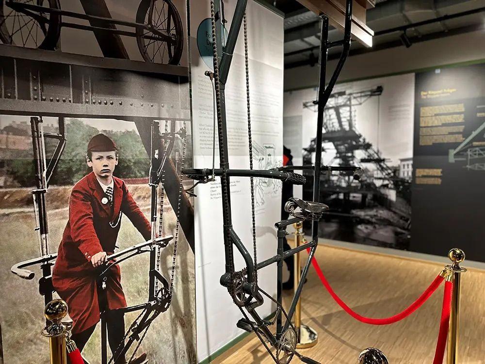 Ein Teil der Ausstellung im Schwebodrom. Ein Junge sitzt auf einem Fahrradähnlichen Gefährt, welches an Schienen aufgehängt ist. 