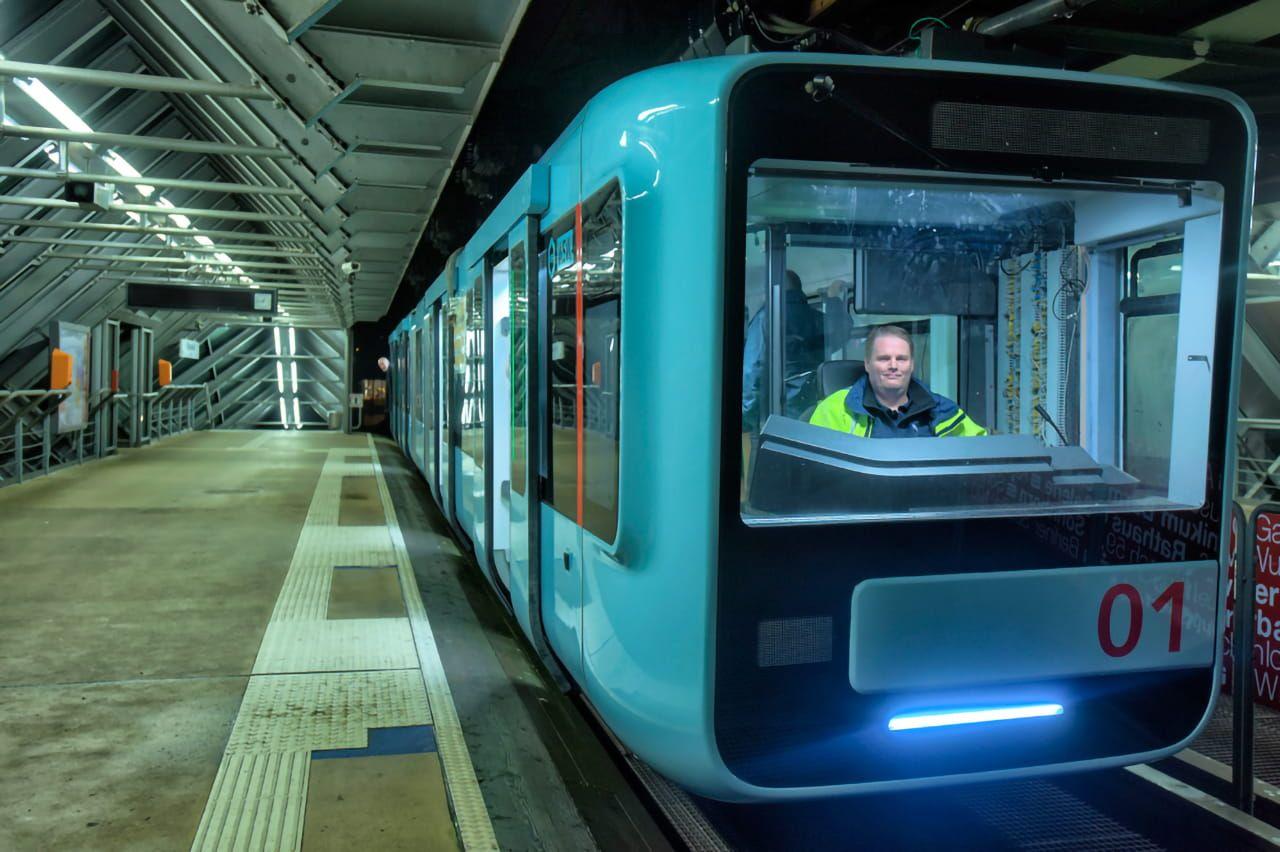 Eine Aufnahme der neuen Schwebebahn in einer Station im Dunkeln. Im Inneren sieht man den Fahrer. 