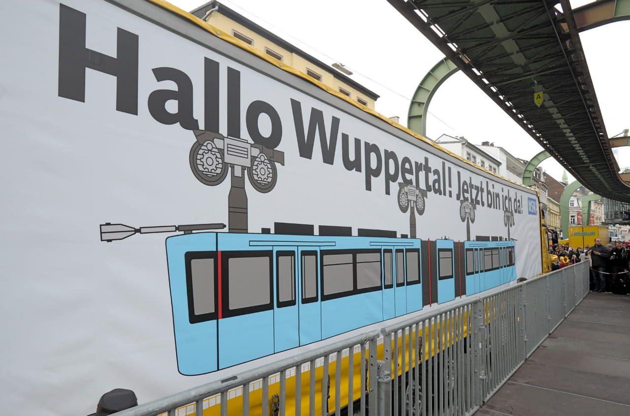 Hallo Wuppertal! Jetzt bin ich da! steht auf der großen Plane, die den ersten neuen Schwebebahnwagen der Wuppertalter Stadtwerke verhüllt